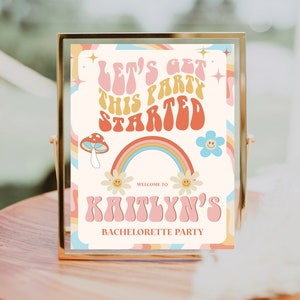 May include: A colorful sign with a rainbow, mushrooms, and flowers. The text on the sign reads "Let's get this party started" and "Welcome to Kaitlyn's Bachelorette Party".