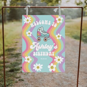 K&ouml;nnte beinhalten: Willkommen zu Ashleys Geburtstagsschild mit einem Regenbogenhintergrund und einer Rollschuhgrafik. Das Schild hat wei&szlig;e G&auml;nsebl&uuml;mchen mit Smiley-Gesichtern darauf.