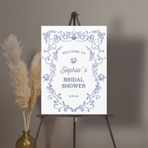 May include: White sign with a blue floral border and the text "Welcome to Sophia's Bridal Shower 01.23.45".
