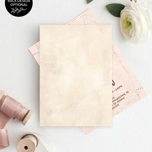 May include: A blank ivory card with a subtle watercolor texture. The card is surrounded by pink and white decorative paper with a rope design. The card is perfect for a wedding invitation or announcement.
