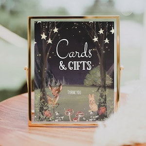 May include: A gold-framed sign with a dark background and twinkling lights. The sign reads "Cards & Gifts" with a deer and rabbit illustration. The text "Thank You" is also included.