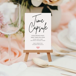 May include: A white card with black text that reads "Time Capsule" and instructions to be opened when the baby turns 18 in 2045. The card is on a small wooden easel.
