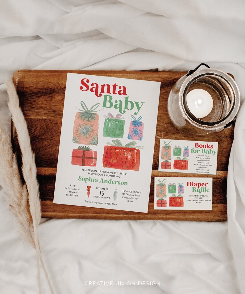 K&ouml;nnte beinhalten: Ein Holztablett zeigt eine "Santa Baby" Babyparty-Einladung mit Aquarell-Geschenkillustrationen. Karten mit der Aufschrift "Books for Baby" und "Diaper Raffle" sind ebenfalls vorhanden. Ein Glaskerzenhalter und dekorative Elemente vervollst&auml;ndigen die festliche Szene.