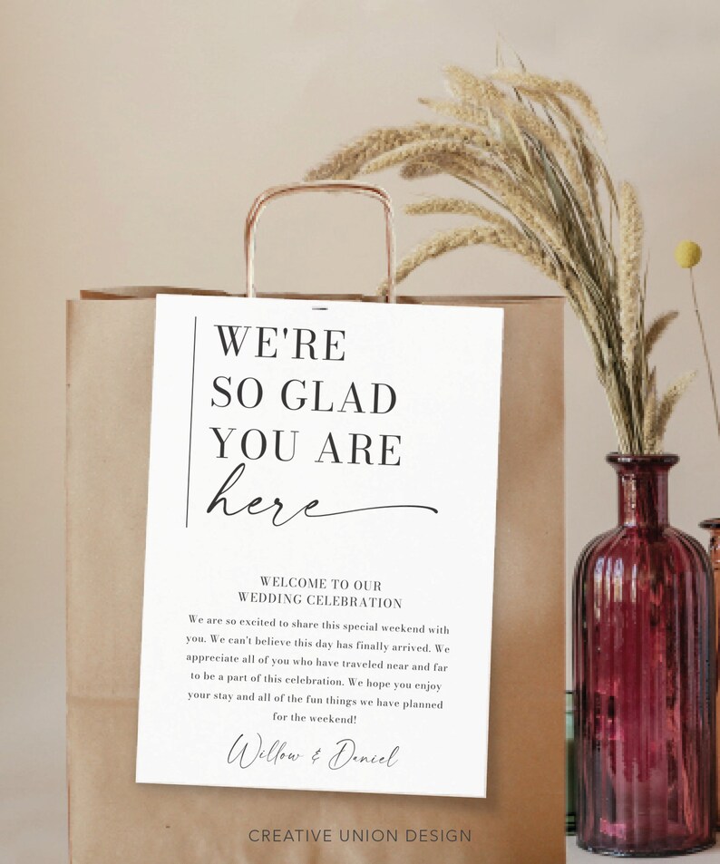 May include: A white sign with black text that reads "We're so glad you are here" and "Welcome to our Wedding Celebration". The sign also includes the names "Willow & Daniel" and the text "Creative Union Design".