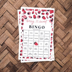 May include: A pink and white bingo card with a strawberry pattern. The card has a title that says "berry & sweet BINGO" and has a list of baby items in each square. The text "FIVE IN A ROW WINS!" is at the top of the card.
