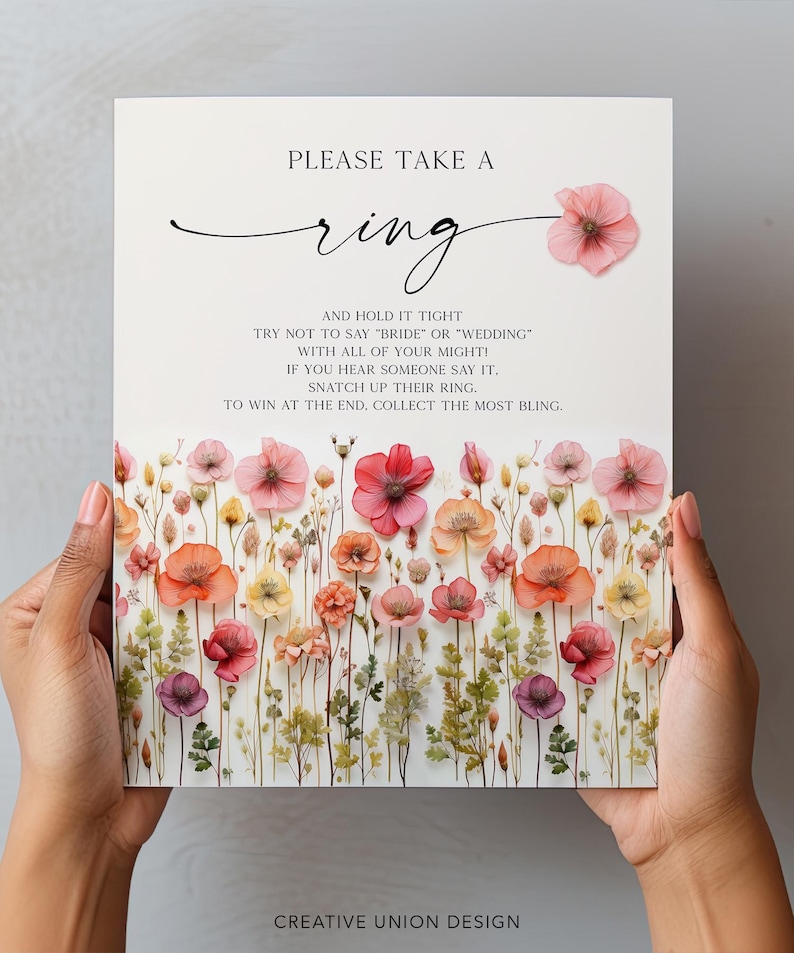 K&ouml;nnte beinhalten: Ein Hochzeitsspielschild mit dem Text "PLEASE TAKE A ring" und Anweisungen. Das Schild ist mit bunten Blumen in Rosa-, Orange- und Gelbt&ouml;nen verziert. Das Schild wird von zwei H&auml;nden gehalten.
