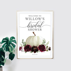 May include: A white pumpkin with a burgundy floral arrangement and the text "Welcome to Willow's bridal shower 06.26.45" on a white background.