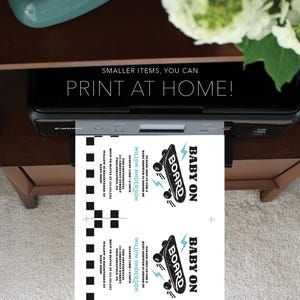 May include: Two printable baby shower invitations featuring a black and white skateboard graphic with the text "Baby on Board". The invitations are printed on white cardstock and have a blue and white chequered pattern on the back.