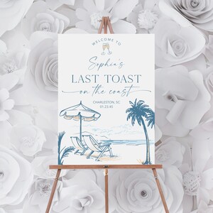 May include: A welcome sign for a last toast party with a blue and white illustration of a beach scene with palm trees, beach chairs, and an umbrella. The text on the sign reads "Welcome to Sophia's Last Toast on the Coast, Charleston, SC 01.23.45".