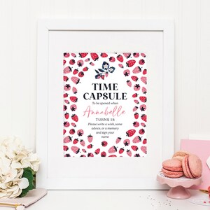 May include: A white framed sign with a strawberry pattern. The sign says "Time Capsule" and "To be opened when Annabelle turns 18. Please write a wish, some advice, or a memory and sign your name."