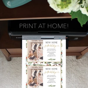 May include: A printer is shown with two holiday cards that read "NEW HOME for the holidays." The cards feature a photo of a woman and child, stockings, and holiday greenery. The text "PRINT AT HOME!" is above the cards.