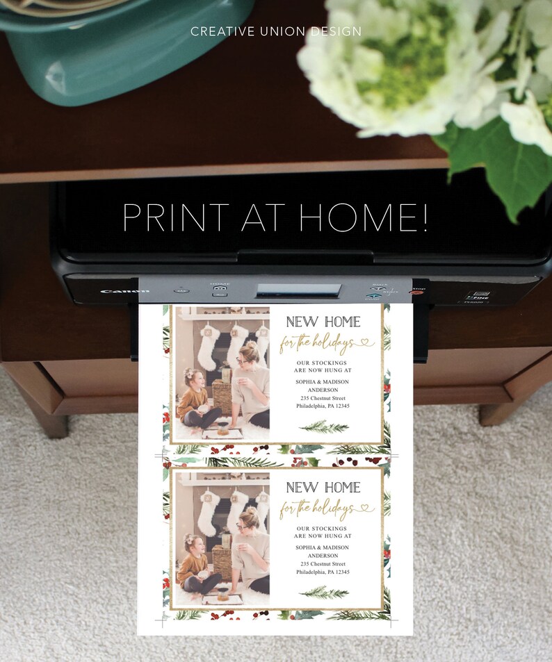 May include: A printer is shown with two holiday cards that read "NEW HOME for the holidays." The cards feature a photo of a woman and child, stockings, and holiday greenery. The text "PRINT AT HOME!" is above the cards.
