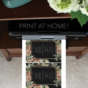 May include: A printer is shown printing two wedding invitations. The invitations have a black background with gold borders and floral and pinecone accents. The text "PRINT AT HOME!" is displayed above the printer.