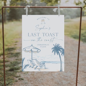 May include: A white sign with blue text that says "Welcome to Sophia's Last Toast on the Coast" with a drawing of a beach scene with palm trees, beach chairs, and an umbrella. The sign also includes the text "Charleston, SC 01.23.45" and "Creative Union Design".
