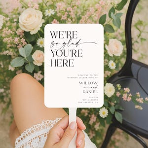 May include: A white rectangular wedding sign with the text "WE'RE so glad YOU'RE HERE". The sign also includes the names Willow and Daniel, the date 01.23.45, and the location MOI GARDENS, Los Angeles, CA.