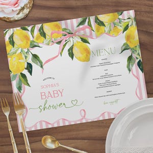 Puede incluir: Un menú de baby shower con un diseño de limón en acuarela. El menú presenta rayas rosas, una cinta rosa y las palabras "Welcome to Sophia's Baby Shower". También se ven utensilios dorados y un plato blanco.