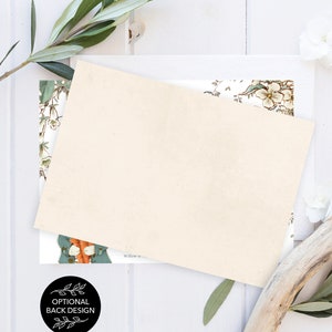Peut inclure: Une carte blanche vierge avec un motif floral au dos. La carte est pos&eacute;e sur une surface en bois blanc avec une branche de verdure et un morceau de bois flott&eacute;.
