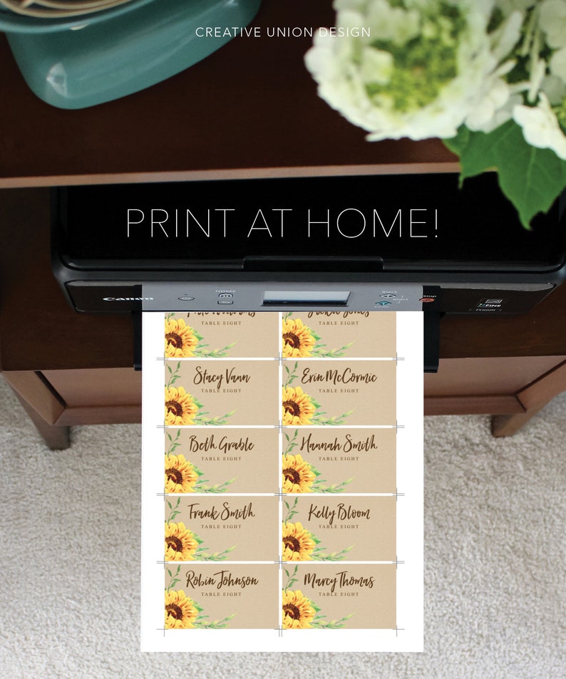 May include: A printer is shown printing eight name cards with sunflower illustrations. The cards have names and the text "TABLE EIGHT". The words "PRINT AT HOME!" are printed above the printer.