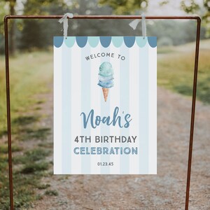 May include: Welcome to Noah's 4th Birthday Celebration sign with a blue and white striped background and an illustration of an ice cream cone with blue and white ice cream. The sign also includes the date 01.23.45.