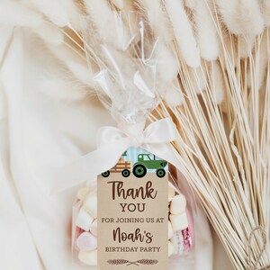 Op de afbeelding: Een transparante cellofaan zak, vastgebonden met een wit lint, gevuld met marshmallows en een label. Op het label staat "Thank You for joining us at Noah's Birthday Party" met een groene tractorafbeelding. Gedroogde tarwestengels staan op de achtergrond.