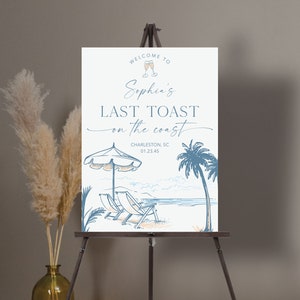May include: A white welcome sign with blue and orange illustrations of a beach scene, palm trees, and deckchairs. The text reads "Welcome to Sophia's Last Toast on the Coast, Charleston, SC 01.23.45".