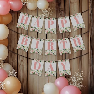 May include: A pink and white floral banner with the words "Happy Birthday" in pink letters. The banner is hanging on a wooden wall with balloons in the background.