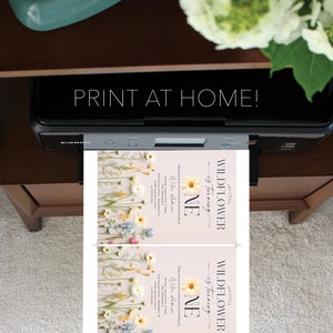 May include: Printable invitation for a first birthday party with a floral theme. The invitation features a light pink background with a floral border and the text "Our Little Wildflower is turning One" in black text. The invitation also includes the child's name and the date of the party.