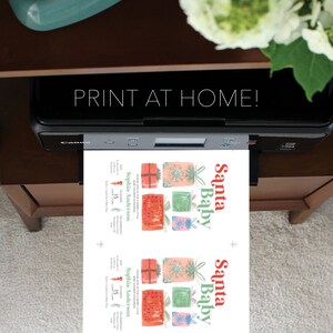 K&ouml;nnte beinhalten: Ein Drucker druckt eine Babyparty-Einladung. Die Einladung zeigt den Text "Santa Baby" in Rot und Gr&uuml;n sowie Aquarellillustrationen von verpackten Geschenken. Der Text "PRINT AT HOME!" wird &uuml;ber dem Drucker angezeigt.