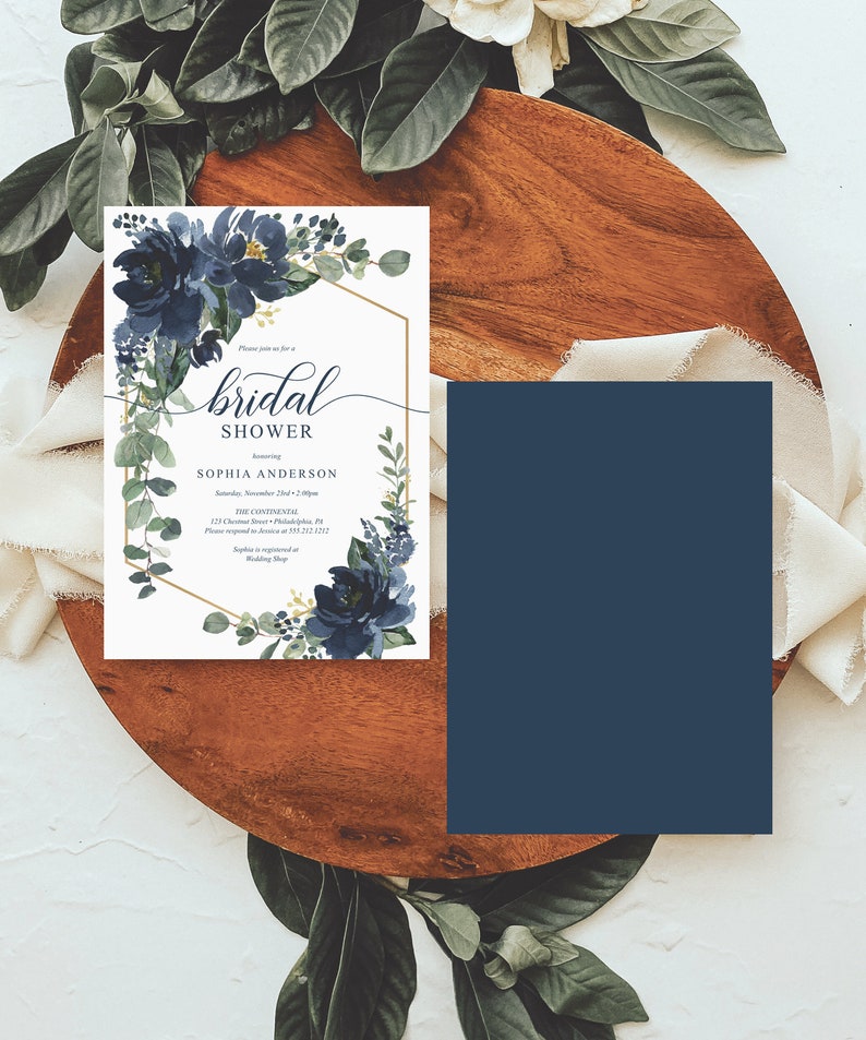 Op de afbeelding: Een uitnodiging voor een bruidsdouche met marineblauwe bloemaccenten en een gouden geometrische lijst. De uitnodiging bevat de tekst "bridal shower" en evenementdetails. Een bijpassende marineblauwe kaart is ook aanwezig.