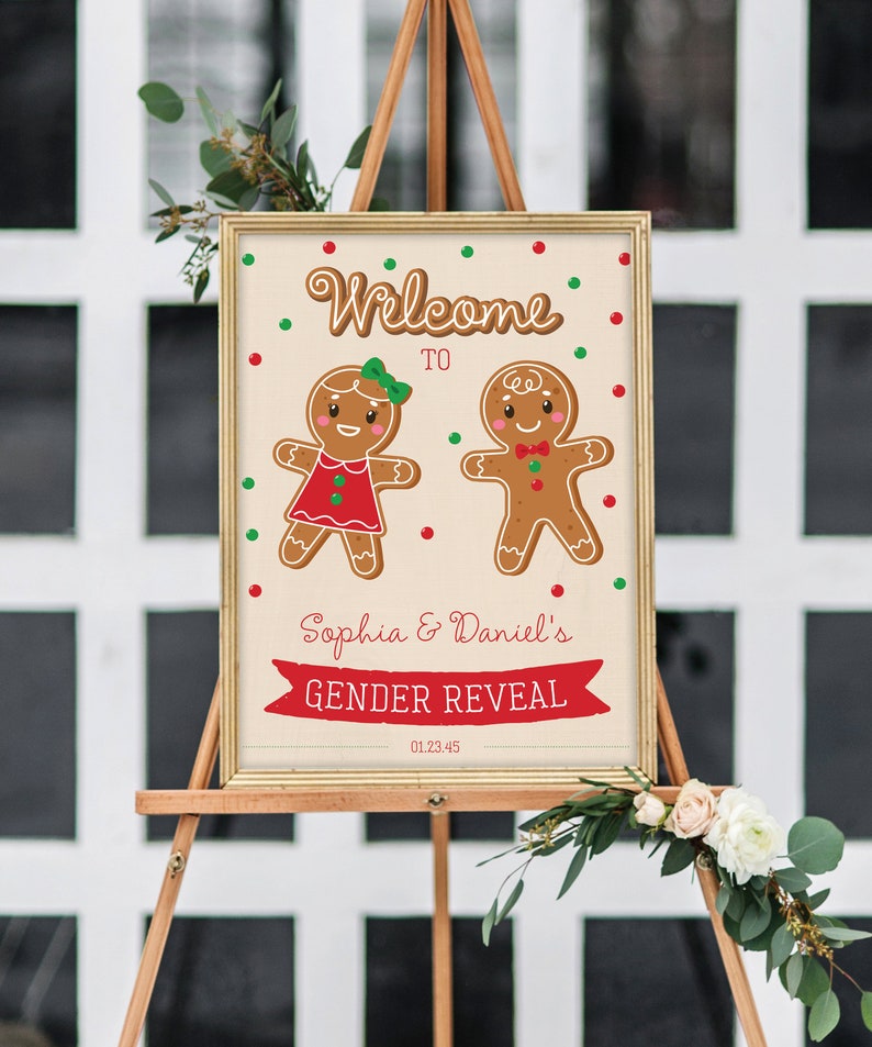 May include: A framed sign on an easel announces a gender reveal for Sophia & Daniel. The sign features gingerbread people and the words "Welcome to" above the names. Red and green dots and a red banner that says "GENDER REVEAL" decorate the sign.