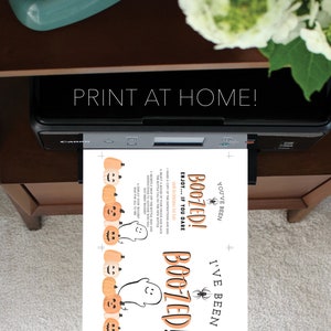 K&ouml;nnte beinhalten: Ein Drucker druckt ein Design zum Thema Halloween. Das gedruckte Blatt zeigt den Text "Boozed!" mit Geister- und K&uuml;rbisgrafiken. Die Worte "Print at Home!" werden &uuml;ber dem Drucker angezeigt.