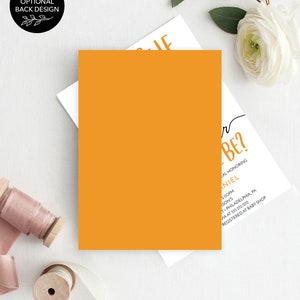 May include: A white card with black text that reads "Q  r BE?"  The card is on a white background with a yellow card and a white flower. The text on the card also reads "A Baby Shower Honoring [Name] 2:00PM [Location] [Address] Registered at Baby Shop"