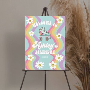 K&ouml;nnte beinhalten: Ein pastellblaues Willkommens-Schild mit Regenbogenstreifen und wei&szlig;en G&auml;nsebl&uuml;mchen. Das Schild lautet "Willkommen zu Ashleys Geburtstag 01.23.45" und zeigt einen Comic-Rollschuh.