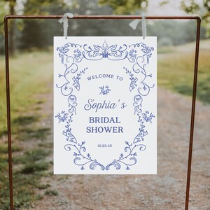 May include: White sign with blue floral border and text that reads "Welcome to Sophia's Bridal Shower 01.23.45".