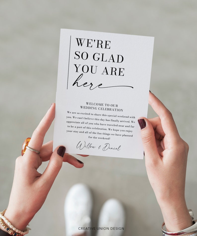 May include: A white card with black text that reads "We're so glad you are here" and "Welcome to our Wedding Celebration". The card also includes a message welcoming guests to the wedding celebration and a signature that reads "Willow & Daniel".