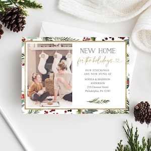 May include: A holiday-themed card with a photo of a family in front of a fireplace. The card features the text "NEW HOME for the holidays" in gold script, surrounded by a festive border of greenery and berries.