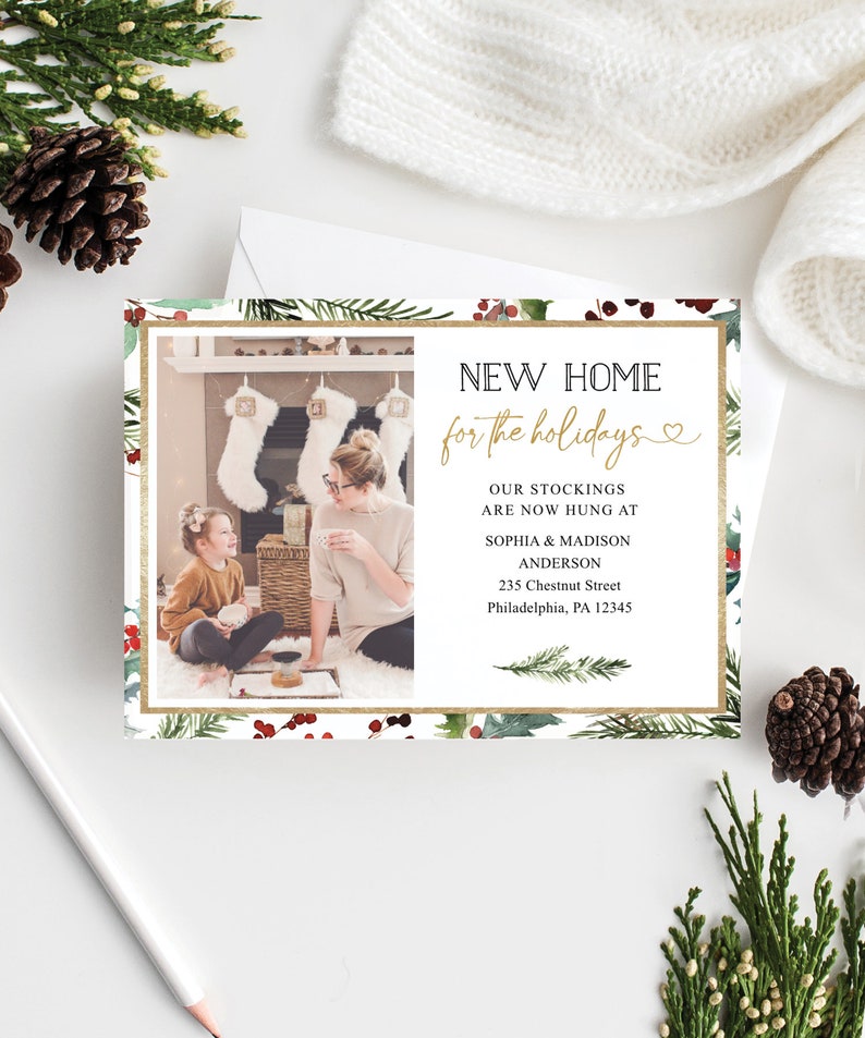 May include: A holiday-themed card with a photo of a family in front of a fireplace. The card features the text "NEW HOME for the holidays" in gold script, surrounded by a festive border of greenery and berries.