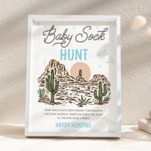 May include: A printable sign for a baby shower game. The sign has a desert landscape with cacti and a sunset. The text on the sign reads "Baby Sock Hunt" and "Baby socks have been hidden throughout the baby shower. Whoever finds the most at the end wins a prize! Happy Hunting."
