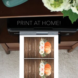 May include: A printer is shown printing two Thanksgiving dinner invitations. Each invitation features an orange pumpkin with floral accents on a wooden background. The text "PRINT AT HOME!" is visible above the printer.