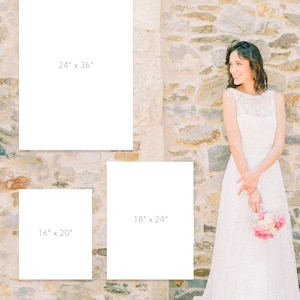 May include: A bride in a white wedding dress holding a bouquet of pink and white flowers stands next to three blank white canvases. The canvases are labeled with the following dimensions: 24" x 36", 18" x 24", and 16" x 20". The background is a stone wall.