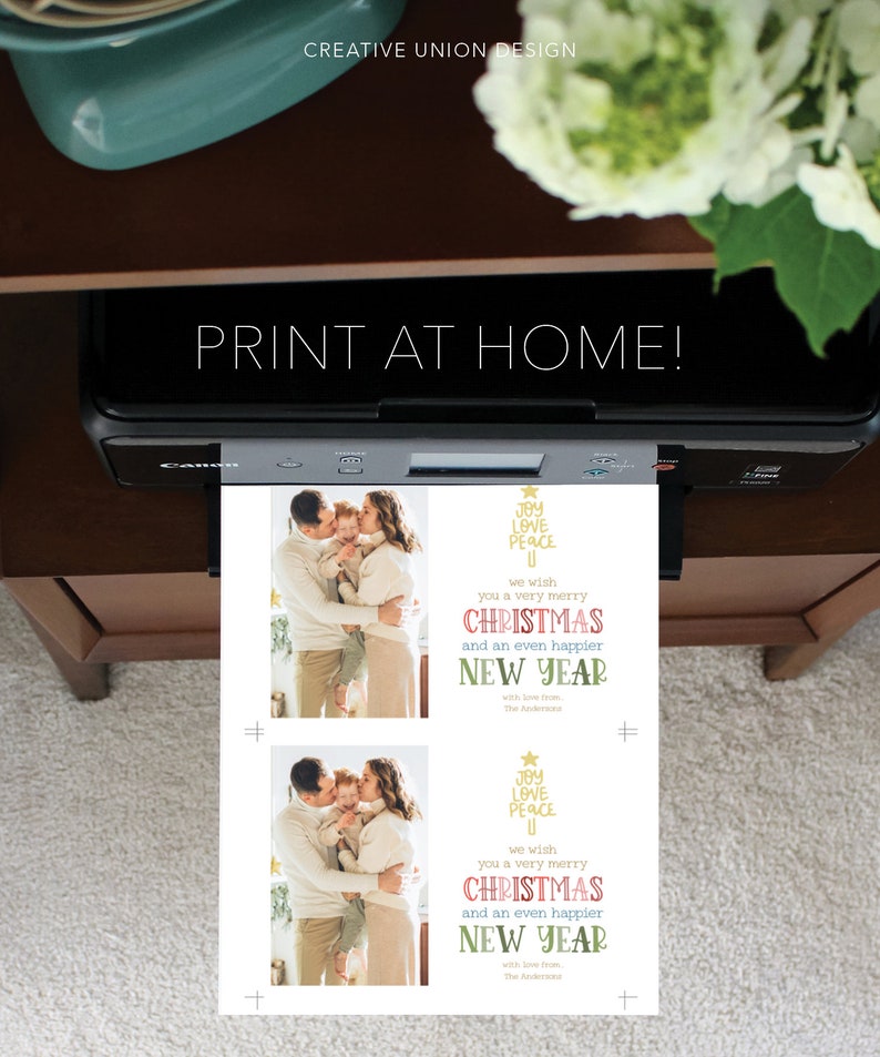 May include: A white sheet of paper emerging from a black Canon printer featuring two identical Christmas card designs. Each card displays a photograph of a family of three and text that reads: JOY LOVE PEACE, we wish you a very merry CHRISTMAS and an even happier NEW YEAR with love from, The Andersons.