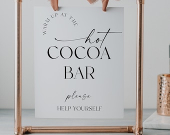 May include: A white sign with black text that reads "Warm Up At The Hot Cocoa Bar Please Help Yourself" on a copper pipe stand with a brown ribbon.