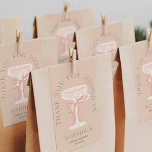 Op de afbeelding: Dank je voor je komst bruiloft douche cadeauzakjes met een roze champagne glas ontwerp en de tekst "Bedankt voor je komst Sophia's Bridal Shower 01.23.45"