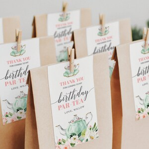 May include: Thank you for coming to my birthday par-tea.  A brown paper bag with a pink and green tea party favor tag featuring a teapot, flowers, and the text "Thank you for coming to my birthday par-tea. Love, Willow".