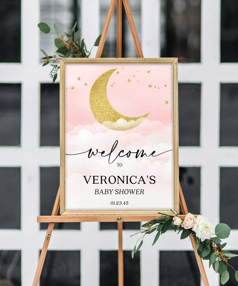 May include: A rectangular sign in a gold frame featuring a pink watercolor sky with a gold glitter crescent moon, clouds, and stars. The text reads: welcome TO VERONICA'S BABY SHOWER 01.23.45. The sign is displayed on a wooden easel.