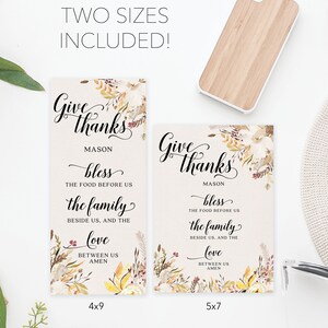 May include: Two rectangular signs with floral accents and the words "Give thanks" in elegant script. The signs include the text "bless the food before us, the family beside us, and the love between us, amen." One sign is 4x9 inches, the other is 5x7 inches.