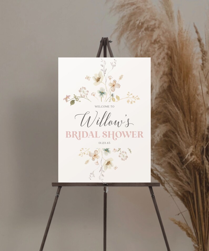 May include: A welcome sign for Willow's bridal shower, displayed on a wooden easel. The sign features floral watercolor illustrations in soft colors and the text "Welcome to Willow's Bridal Shower" in elegant script and a light pink font. The date 01.23.45 is also included.