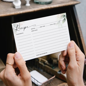 May include: A blank recipe card with a watercolor design of green leaves and gold accents. The card has lines for writing ingredients, directions, serves, prep time, and total time. It also has a space for "From the Kitchen of".
