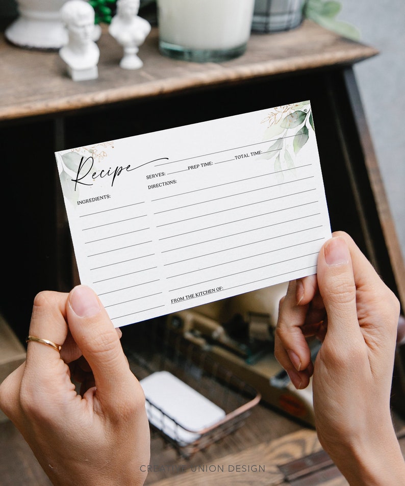 May include: A blank recipe card with a watercolor design of green leaves and gold accents. The card has lines for writing ingredients, directions, serves, prep time, and total time. It also has a space for "From the Kitchen of".