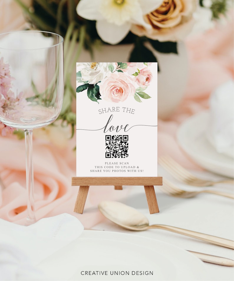 K&ouml;nnte beinhalten: Ein kleines Holzstaffelei h&auml;lt ein Schild mit floralen Akzenten und den Worten "Share the Love". Unter dem Text befindet sich ein QR-Code. Das Schild steht auf einem Tisch mit einem Glas und Besteck.
